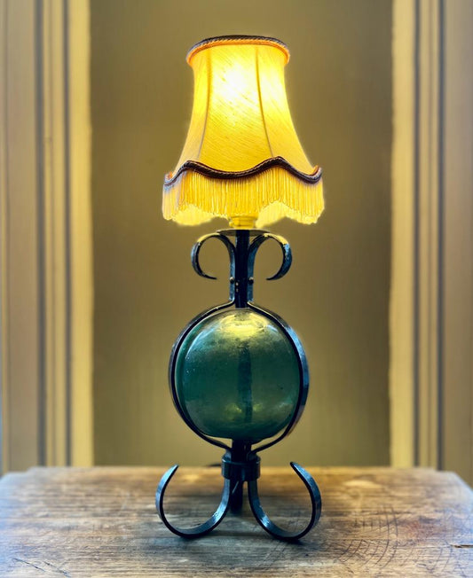 Elevate the ambience of your space with our unique Table Lamp. Featuring a sleek Nautical style and a antique glass fishing bouy, this lamp adds a touch of sophistication to any room. Encased in an intricate mid century metal frame. 